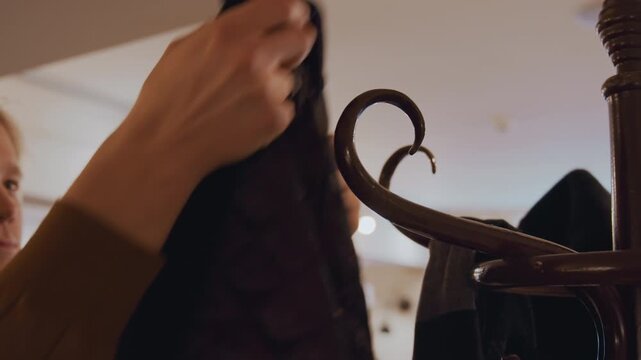 Close up of young man examining and handling clothing items in indoor retail environment. man interacts with garments focusing on texture details while surrounded by soft lighting fixtures