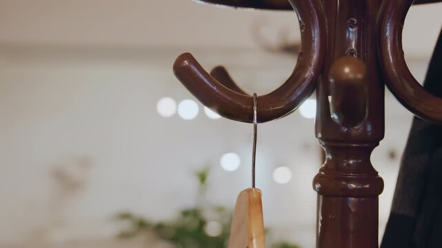 Close up of hand placing wooden hangers on metal hooks attached to antique coat rack. background features soft lighting and blurred decorative elements emphasizing texture detail of polished