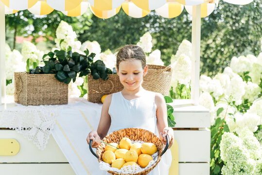 Smiling young girl Holding wicker basket filled with fresh lemons outdoors in a bright summer garden setting.