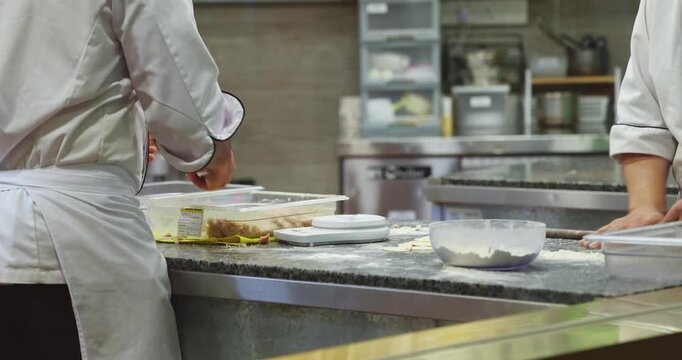 Chefs preparing handmade dumplings in professional restaurant kitchen, culinary staff working with dough and filling, commercial food production.