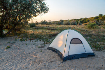 A tent on a sandy beach near a tree. Weekend camping. © Vladislav