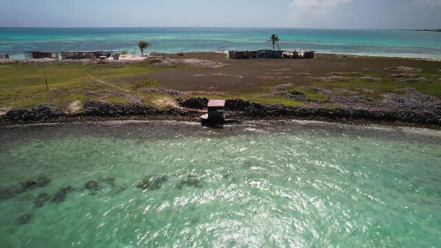 Aerial view of a small wooden shack on the coastline of the Los Roques archipelago with turquoise waters and clear skies in Los Roques, Dependencias Federale, Venezuela.