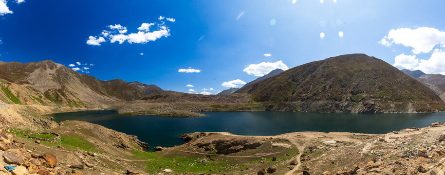 View of Lulusar Lake surrounded by rugged mountains, rocky terrain, and green patches under a bright blue sky in Balakot, Khyber Pakhtunkhwa, Pakistan.