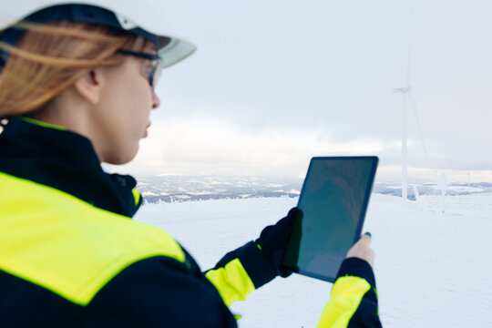 Woman in high visibility jacket using tablet near windmills in winter landscape