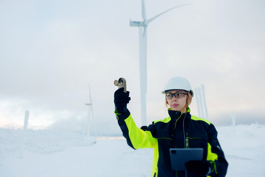 Woman engineer in safety gear measures wind speed at a snowy wind farm