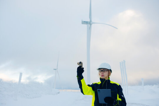 Woman engineer checks wind turbine performance in a snowy, cold environment