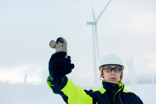 Woman engineer in high visibility jacket checks wind turbine performance with anemometer