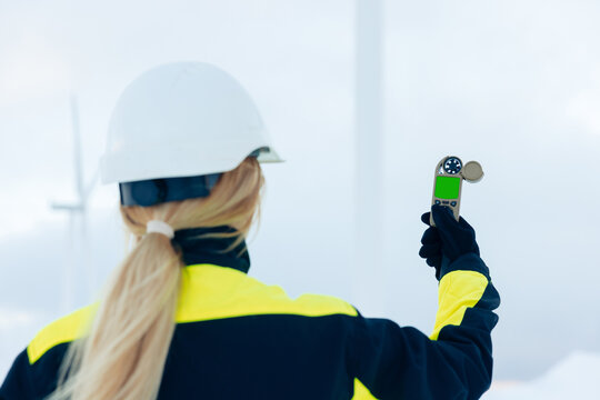 Woman in hard hat and high-visibility jacket measures wind speed with anemometer