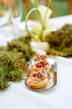 A row of bite-sized canap&eacute;s on a silver tray sits amid moss and plant d&eacute;cor, creating a natural, sophisticated appetizer display perfect for weddings, parties, and upscale catering events.