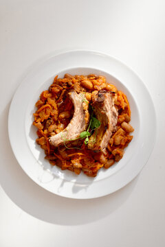 Tender braised ribs sit atop a hearty bean and carrot stew on a clean white plate. Fresh greens garnish add color and rustic, comforting vibe suitable for home meals or restaurant menus.