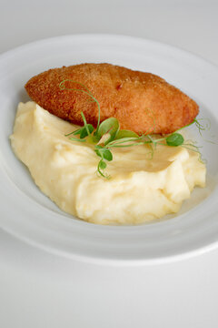 Crispy golden croquette rests on smooth mashed potatoes, accented by delicate microgreens for a refined, restaurant-quality presentation perfect for premium menus and food stock imagery.