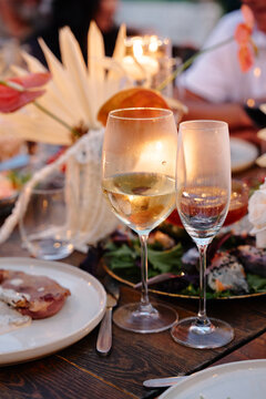 Soft candlelight reflects in two wine glasses on an elegant dinner table, creating a warm, intimate atmosphere for a romantic celebration with food, flowers and relaxed evening entertaining.