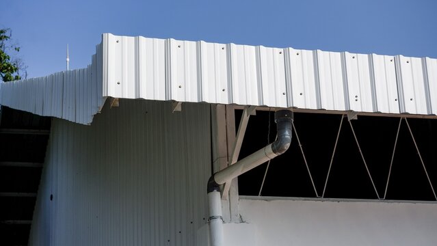 Modern steel building exterior showing white metal roofing panels and rainwater gutter system in daylight.