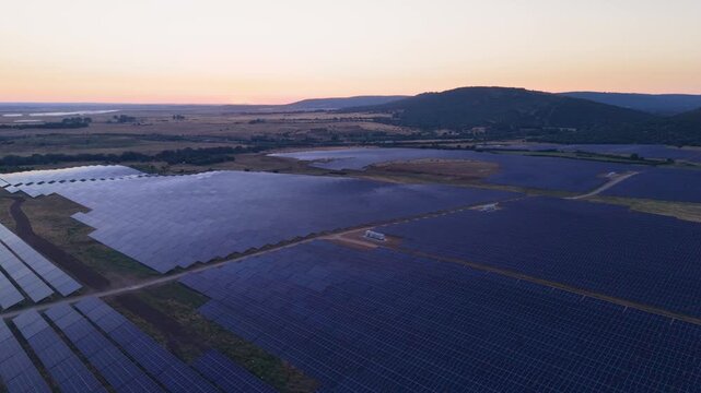 Aerial view of a vast solar farm with rows of photovoltaic panels stretching across the rural landscape under a soft sunset sky in Ciudad Rodrigo, Castile and Leon, Spain.