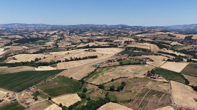 Expansive aerial of golden harvested fields green crops farms villages and rolling hills under clear sky