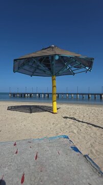 ​Yellow Wooden Beach Umbrella with Pier Dock Stretch into the Calm Ocean Water on Sandy Beach in Montecristi, Dominican Republic, Vertical 4K Video