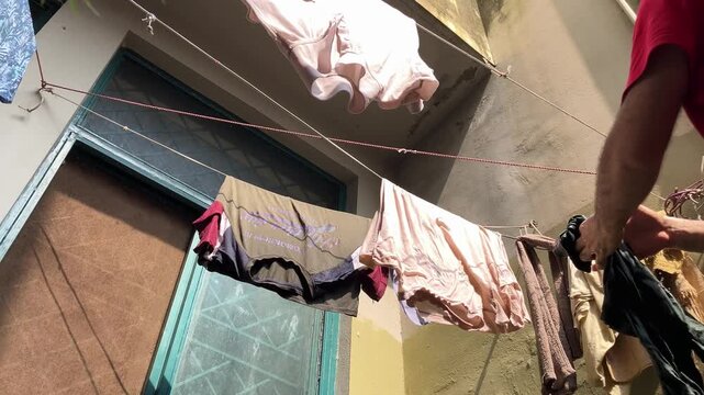 Adult man hanging wet clothes on a clothesline wire outdoors after washing