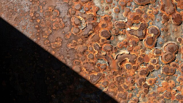 Close-up of corroded metal surface with heavy rust pitting and diagonal shadow
