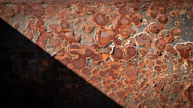 Close-up of corroded metal surface with circular rust patches and sharp shadow