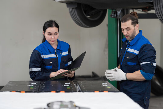 Electric vehicle car auto services. EV garage. Diagnostic battery pack. Mechanic discussion and diagnosing electric car vehicles battery, component checks at auto workshop
