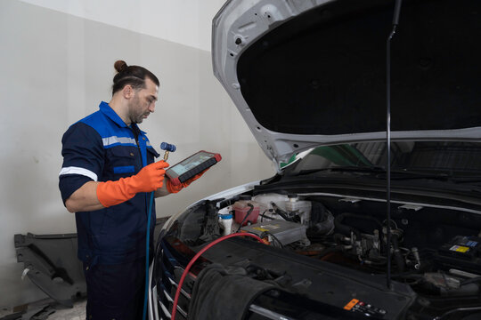Male mechanic diagnosing battery under hood of car at the garage. Mechanic examining, repair and maintenance automotive electrical systems at auto car repair service