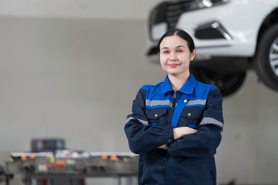 Electric vehicle car auto services, EV garage. Female car mechanic standing wear work uniform and crossed arms in auto workshop