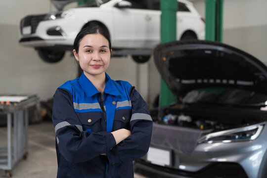 Electric vehicle car auto services, EV garage. Female car mechanic standing wear work uniform and crossed arms in auto workshop