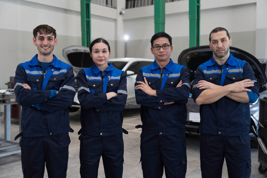 Electric vehicle car auto services, EV garage. Team of mechanic and electrician standing wear work uniform and crossed arms preparing for work in auto workshop