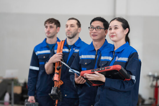 Electric vehicle car auto services, EV garage. Team of mechanic and electrician standing wear work uniform and holding equipment tools for work in auto workshop