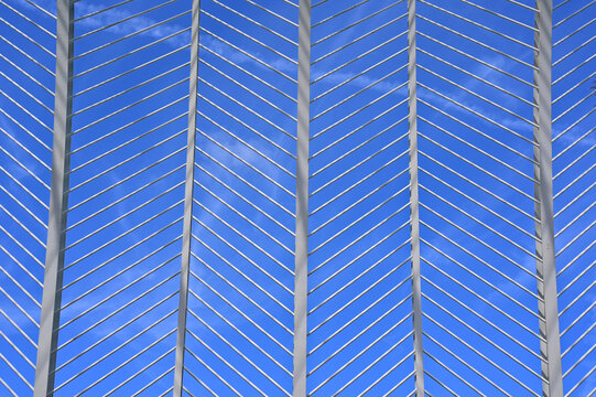 decorative arching open web exterior structural steel frame. curved I beams and diagonal round or circular section bracing members. perspective view looking up. crisp blue sky background.    