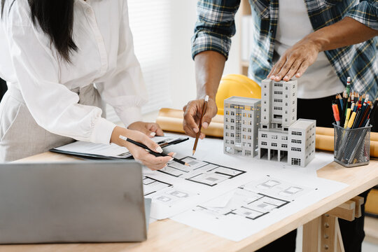 Architectural Planning in Collaboration: Two professional architects reviewing blueprints and a scale model of a building project, working together to finalize structural details in an office setting.