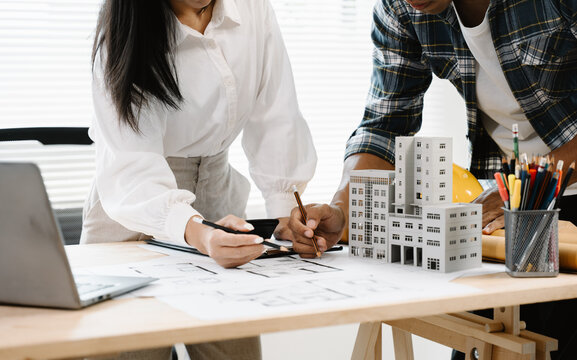 Architectural Collaboration: Two professionals meticulously examine building blueprints and a miniature architectural model, symbolizing focused teamwork and design innovation.