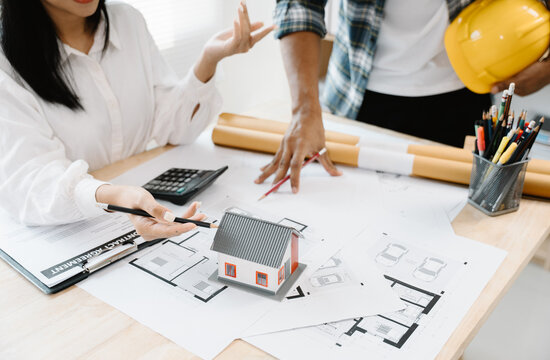 Architectural Collaboration: Two architects discuss blueprints and a miniature house model, symbolizing planning and development in the construction industry.