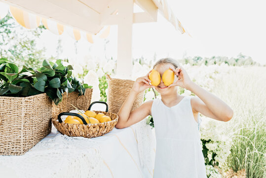 Smiling young girl Holding wicker basket filled with fresh lemons outdoors in a bright summer garden setting.
