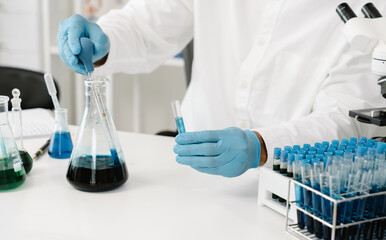 Fototapeta premium Doctor hand taking a blood sample tube from a rack with machines of analysis in the lab background, Technician holding blood tube test in the research laboratory.