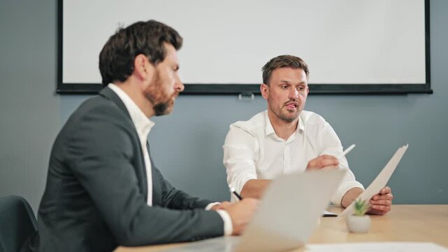 Two business professionals review documents and discuss project details. Collaboration is evident as insights are shared, fostering teamwork and strategic decision-making in corporate setting.