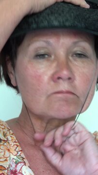 An elderly woman pulls a vintage hat with an elastic strap under the chin onto her head.. vertical video.