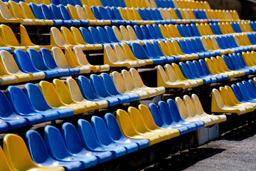 Fototapeta premium Rows of empty blue and yellow plastic seats at sports stadium, sunny spectator stands before match or tournament Photo