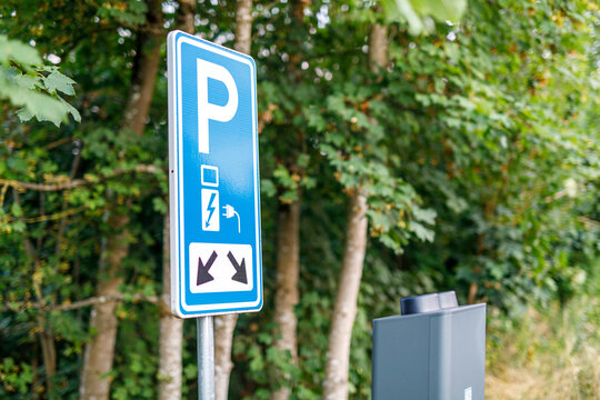 Blue sign indicating parking for electric vehicles with charging station in a green outdoor setting.