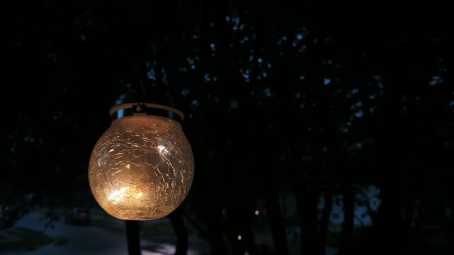 A glowing lantern sways in the wind on a stormy night in a residential neighborhood 