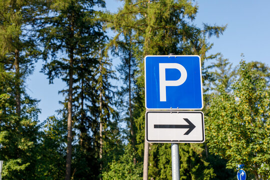 Blue parking sign with a white 'P' and a right-pointing arrow, framed by green trees and blue sky.