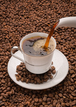 View of coffee being poured into a white porcelain cup surrounded by roasted coffee beans in Islamabad, Islamabad Capital Ter, Pakistan.