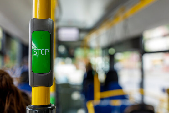 Close-up of a green stop request button inside a public bus or tram, with blurred passengers.