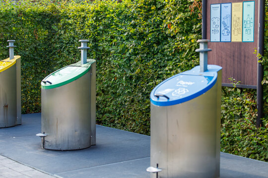 Sleek outdoor recycling bins for paper, glass, and general waste against a vibrant green hedge.