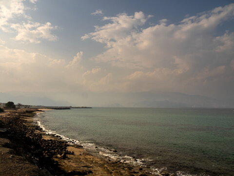View of the rocky coastline and calm sea with distant mountains under a cloudy sky in Ras Al-Khaimah, Ras Al Khaimah, United Arab Emirates.
