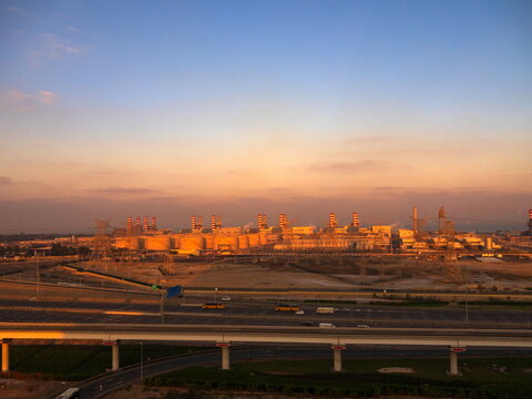 View of the Dubai Electricity and Water Authority power plant at sunset with industrial structures, power lines, and a highway in the foreground in Dubai, Dubai, United Arab Emirates.