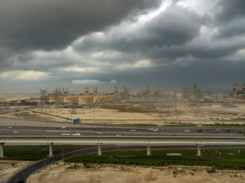 View of the Dubai Electricity and Water Authority power plant with industrial infrastructure and a highway under a dramatic cloudy sky, Dubai, Dubai, United Arab Emirates.