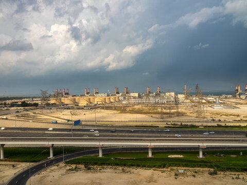 View of the Dubai Electricity and Water Authority power plant with industrial storage tanks, smokestacks, power lines, and highway under dramatic clouds in Dubai, Dubai, United Arab Emirates.