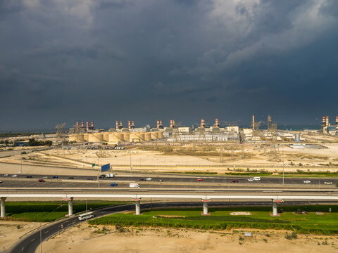 View of the Dubai Electricity and Water Authority power plant complex with industrial chimneys, storage tanks, and power lines under a dramatic cloudy sky in Dubai, Dubai, United Arab Emirates.
