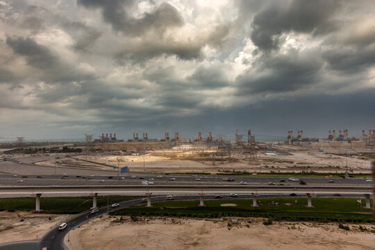 View of the Dubai Electricity and Water Authority power plant complex under a dramatic cloudy sky with a highway and desert landscape in the foreground in Dubai, Dubai, United Arab Emirates.